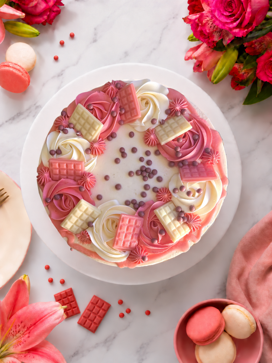 Overhead view of Blush Pink Celebration Drip Cake topped with eight pink and white mini chocolate bars, buttercream swirls and pearls.