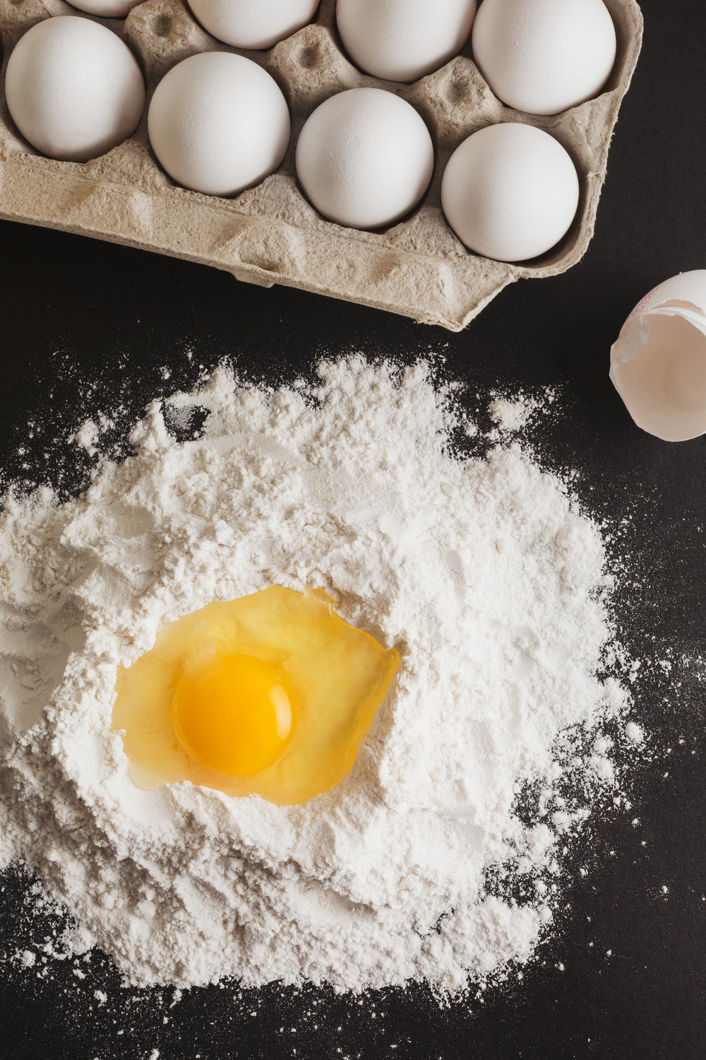 cracked-egg-resting-in-well-of-flour-on-black-counter