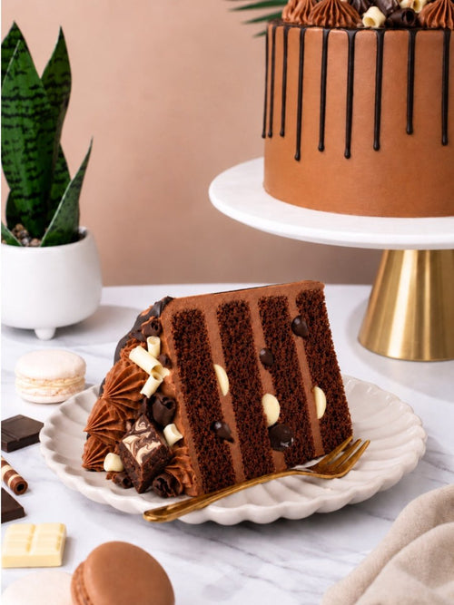 Slice of Indulgent Chocolate Celebration Cake showing layers of chocolate sponge and buttercream, with a brownie bite and chocolate curls