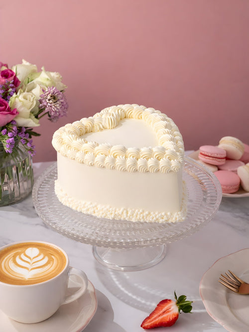 Vintage Heart Cake in cream buttercream with a piped shell border, on a glass stand with a coffee